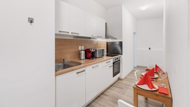 A modern kitchen with white cabinets, a microwave, a kettle, and a dining table set with red napkins and glasses. - Prague Serenity Suite Apartworld (Praha)
