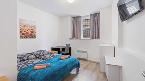 A small, clean room with a bed, a desk, a chair, a TV, and a window with curtains. - Prague Serenity Suite Apartworld (Praha)