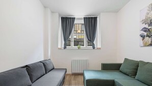 A room with a grey sofa, a green sofa, a radiator, and a window with curtains. - Prague Serenity Suite Apartworld (Praha)