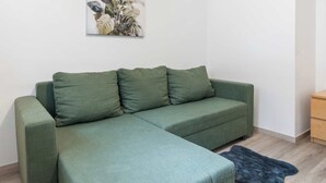A green sectional sofa with a dark rug, a wooden floor, and a wall-mounted plant. - Prague Serenity Suite Apartworld (Praha)