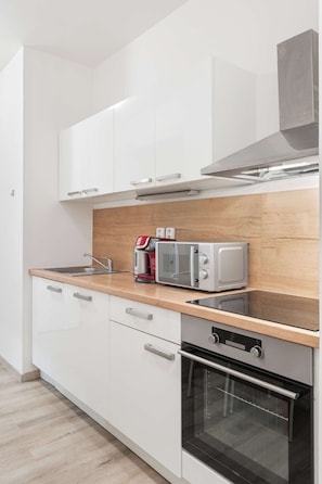 Eine moderne Küche mit weißen Schränken, einer Holzarbeitsplatte, einem eingebauten Backofen, einer Mikrowelle und einer Kaffeemaschine.