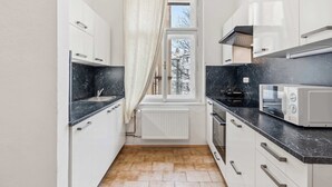 Ett smalt kök med vita skåp, en svart bänkskiva, en mikrovågsugn och ett fönster med en gardin.