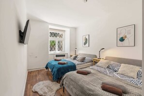 Ein Schlafzimmer mit zwei Betten, einem Fenster, einem an der Wand befestigten Fernseher und Kunstwerken.