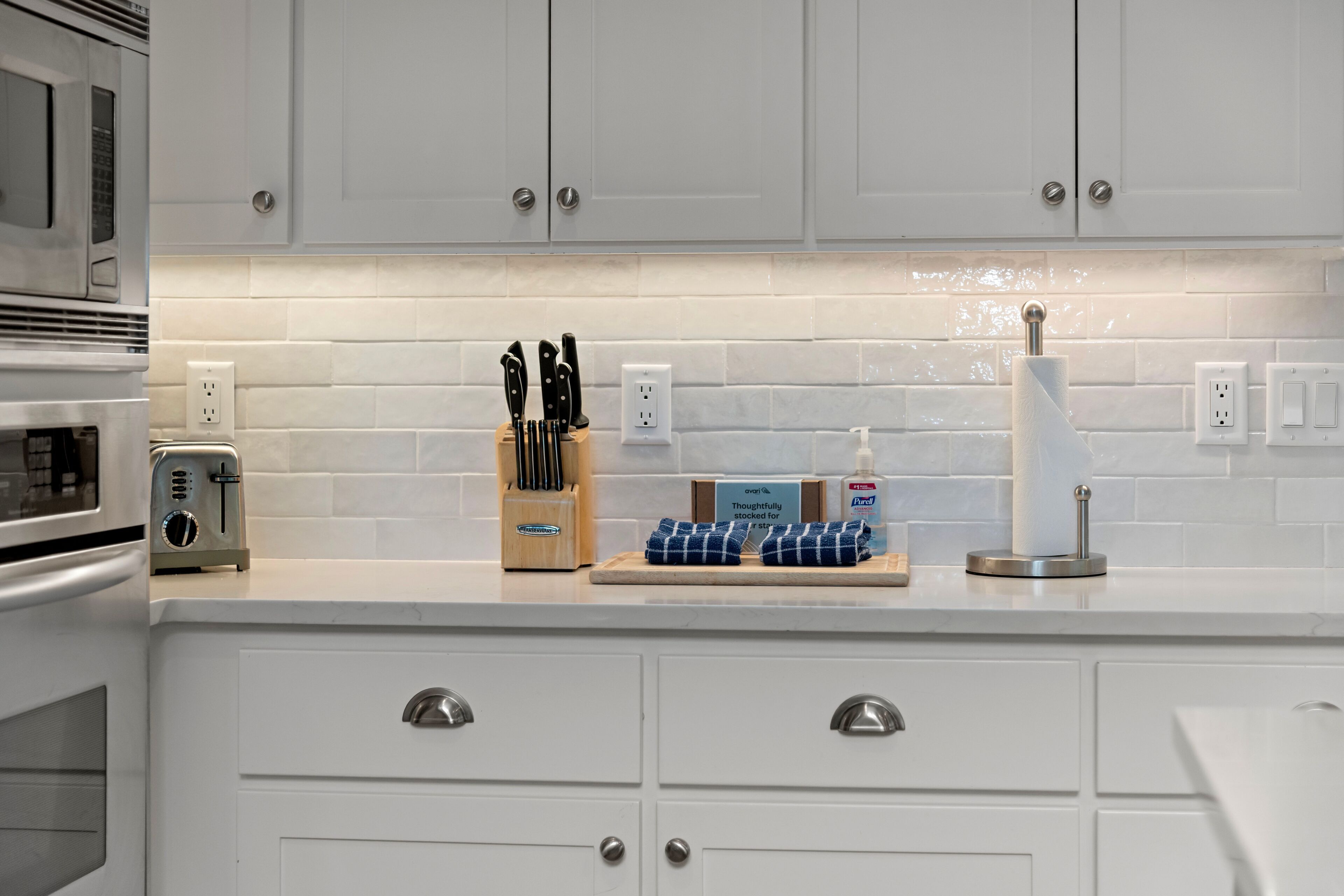 A kitchen with white cabinets, a toaster, a knife block, and a paper towel holder.