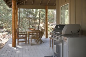 Een terras buiten met een barbecue, houten stoelen en een tafel gedekt met eten.