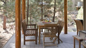 Eine Holzterrasse im Freien mit Tisch und Stühlen, umgeben von Bäumen.