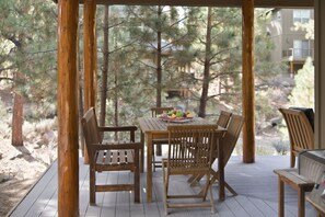 Eine Holzterrasse im Freien mit Tisch und Stühlen, umgeben von Bäumen.