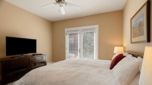 Ein Schlafzimmer mit einem Bett, einem Fernseher auf einer Holzkommode, einem Deckenventilator und einem Fenster mit Jalousien.