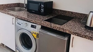 Eine kompakte Küche mit Waschmaschine, kleinem Kühlschrank, Mikrowelle und Spüle.