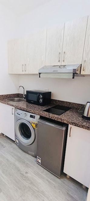 Eine kompakte Küche mit Waschmaschine, kleinem Kühlschrank, Mikrowelle und Spüle.