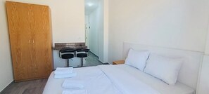 A hotel room with a bed, a wooden wardrobe, two black bar stools, and a small table. - Beach & Pool Escape | Stylish Studio +Balcony (hurghada)