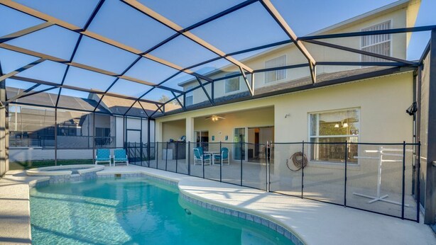 Una piscina con un recinto in vetro, una zona patio coperta e un edificio con tetto piatto.