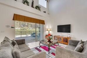 Ein Wohnzimmer mit einer Couch, einem Couchtisch, einem Fernseher und einer Glastür, die zu einem Außenbereich führt.