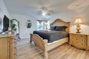 Ein Schlafzimmer mit einem Bett, einem Deckenventilator, einer Nachttischlampe, einem Schminktisch und einem Spiegel.