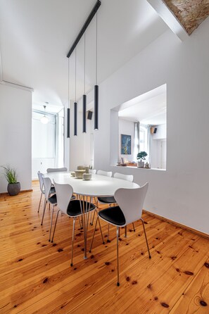 A modern dining area with a round table, white chairs, hanging pendant lights, and a wooden floor. - Stylish High-End Apartment with Direct Elevator Access (Berlin)