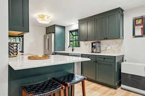 A kitchen with dark green cabinets, a marble countertop, a stainless steel refrigerator, and a built-in stove.
