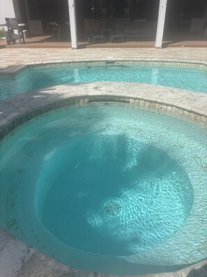 Ein Schwimmbecken mit klarem Wasser, einer Steinkante und Liegestühlen im Hintergrund.