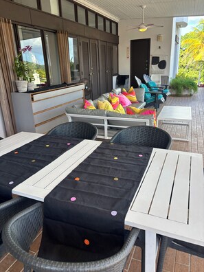Ein moderner Außenbereich mit einer Sitzecke, einer Couch, Stühlen, einem Tisch und einem Deckenventilator.