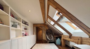 Ein Schlafzimmer im Spitzboden mit schrägem Dach, Holzbalken, einem Hängesessel und einem kleinen blauen Hausmodell.