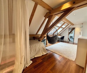 Ein Schlafzimmer mit Holzbalkendecke, einem Hängesessel, einem Bett und einem Schreibtisch.