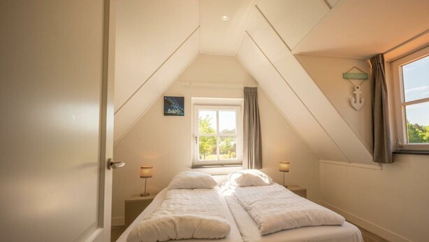 A bedroom with two beds, a window with curtains, a picture on the wall, and a small table with a lamp.