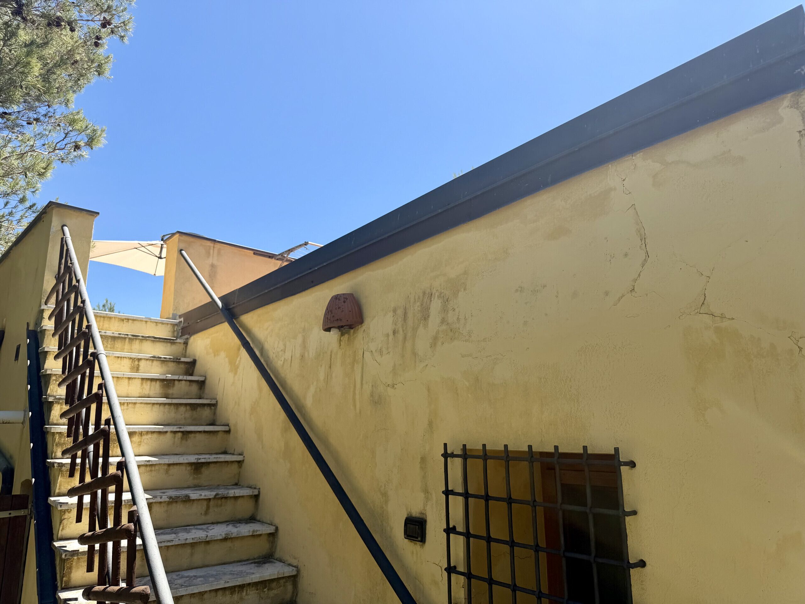 A staircase leading to a building with a yellow wall, a metal railing, and a barred window.