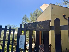 A wooden sign with 'Au Pir' written on it, a wooden fence, and a building with a beige exterior. - Villetta Au Pin - Peace and Relaxation in Lingueglietta’s Pine Forest with Ocean Views and Stunning Valleys, by HOST4U (Lingueglietta)