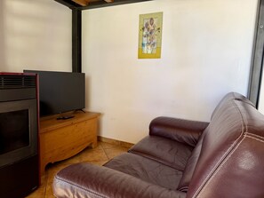 A living room with a brown leather sofa, a television on a wooden cabinet, and a painting on the wall. - Villetta Au Pin - Peace and Relaxation in Lingueglietta’s Pine Forest with Ocean Views and Stunning Valleys, by HOST4U (Lingueglietta)
