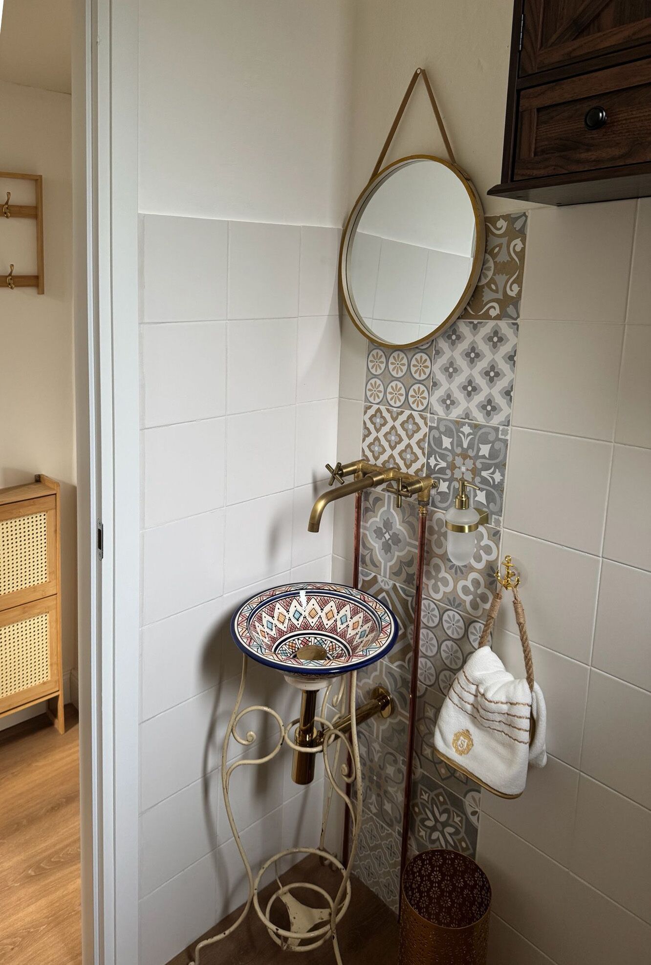 Un baño con pared de azulejos blancos, un espejo redondo, un lavamanos decorativo y una toalla colgada.
