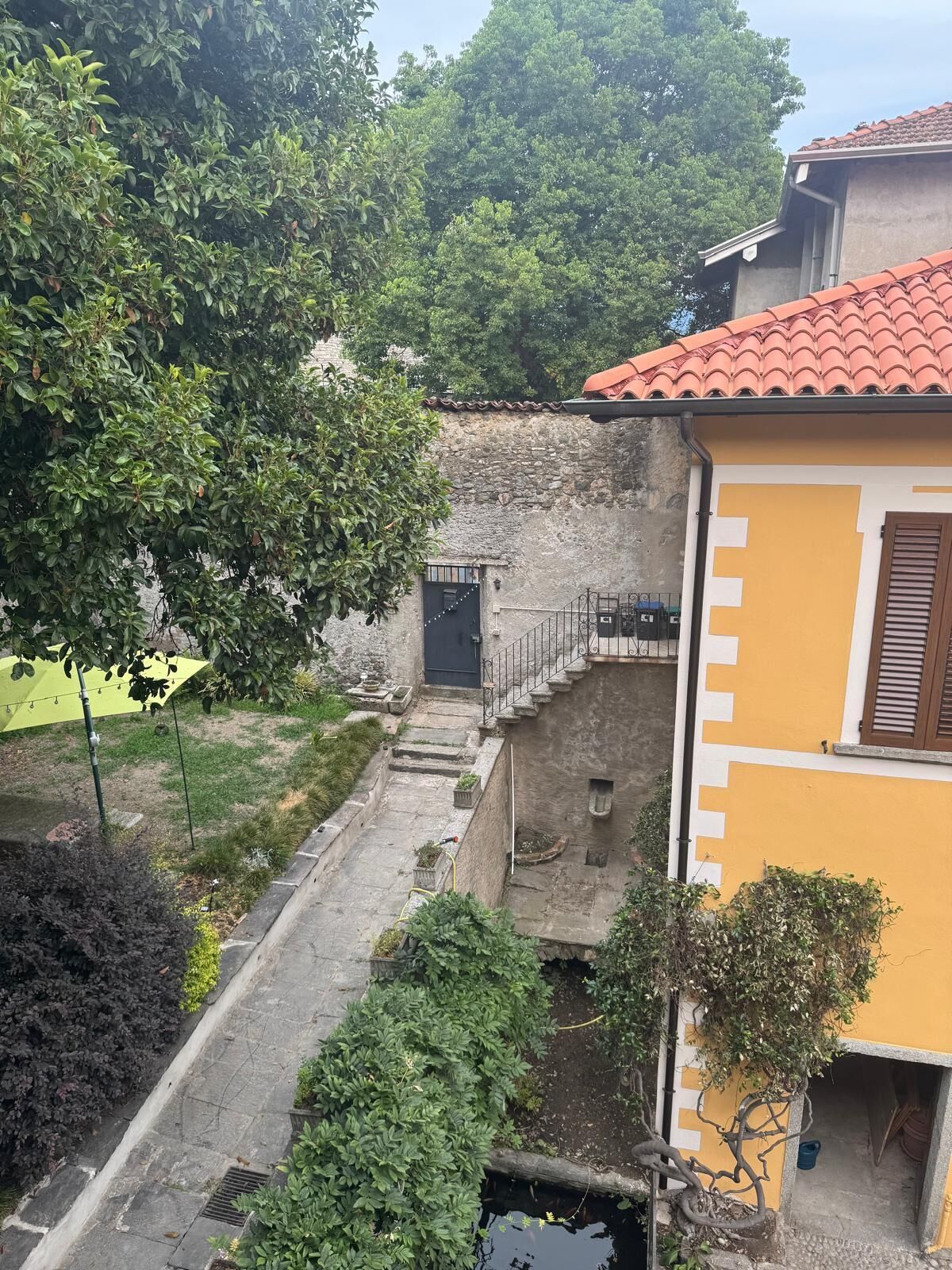 A courtyard with a stone wall, a small garden, and a building with a red-tiled roof.