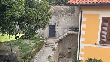 A courtyard with a stone wall, a small garden, and a building with a red-tiled roof.