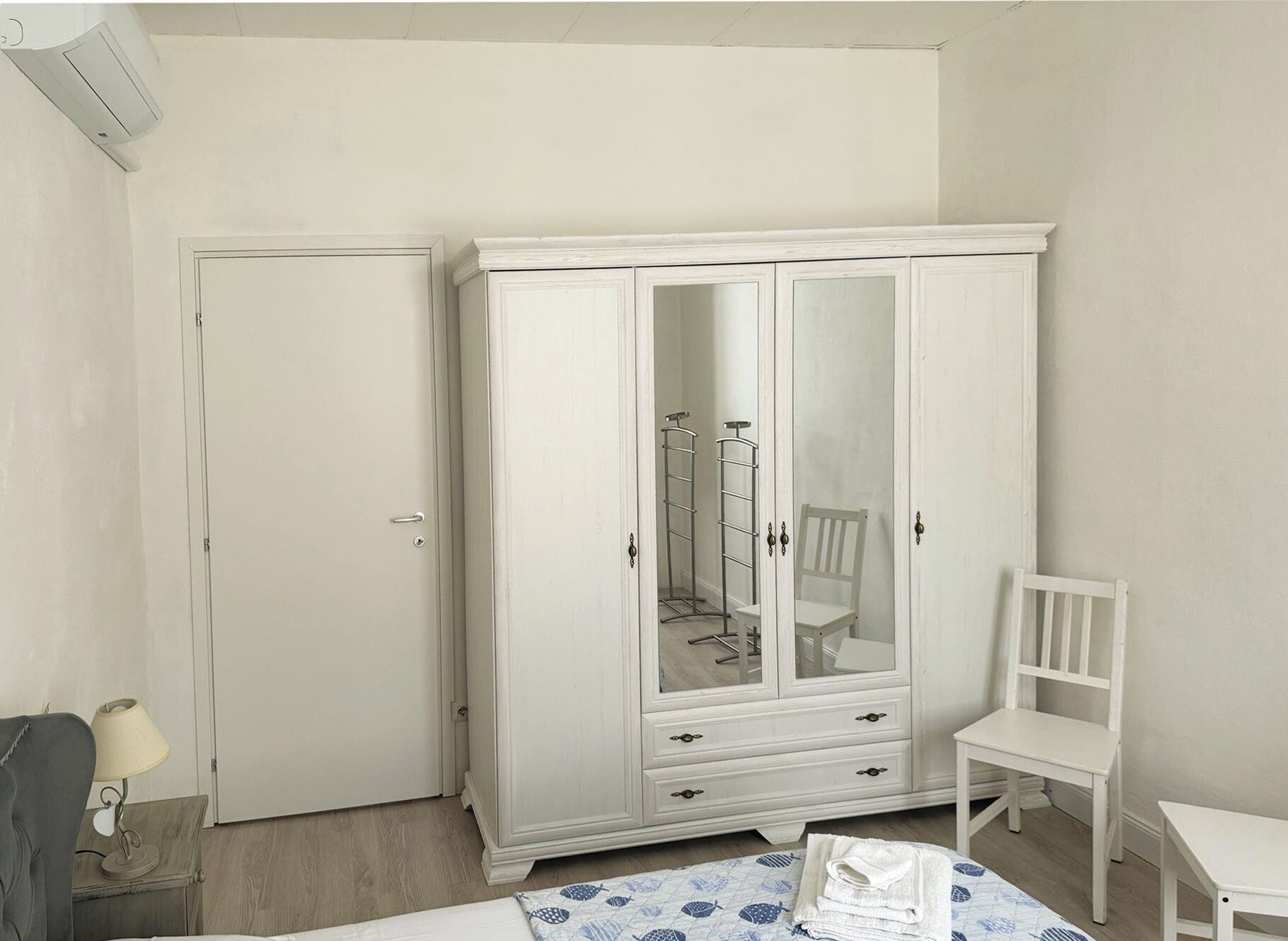 Een kamer met een witte kast, een stoel, een klein tafeltje en een bed.