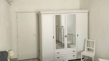 Een kamer met een witte kast, een stoel, een klein tafeltje en een bed.