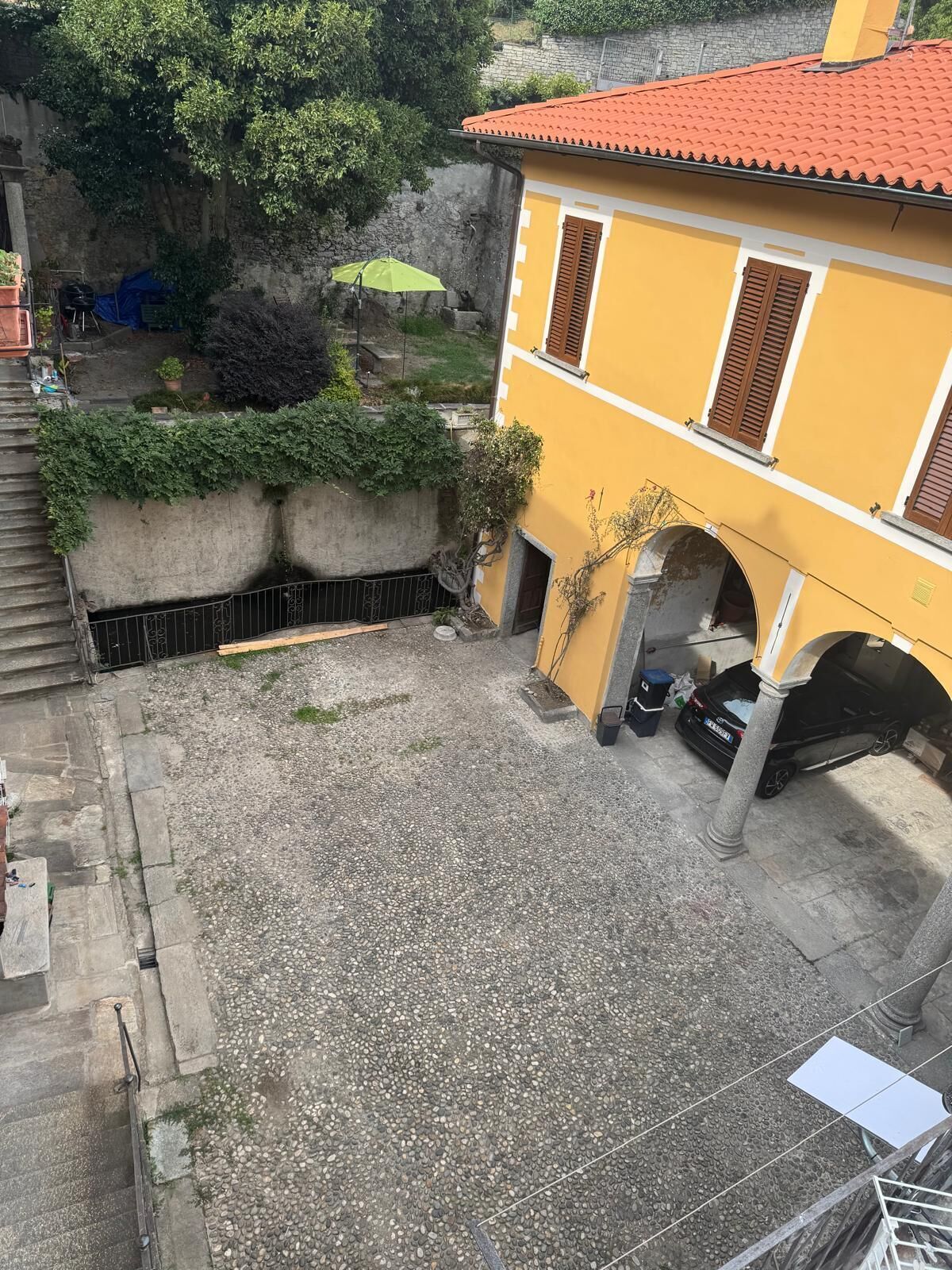 A courtyard with a yellow building, a stone wall, and a gravel ground.