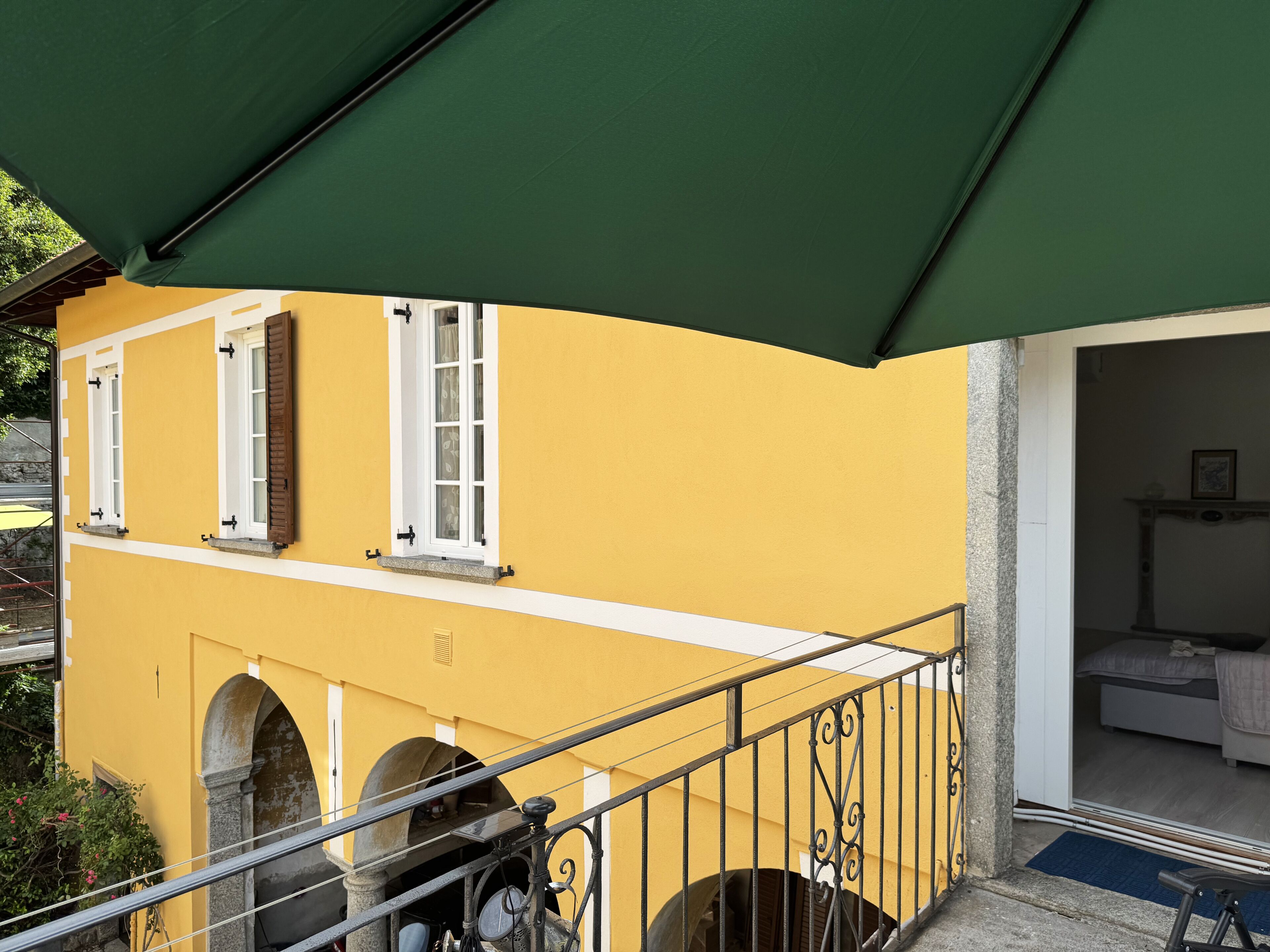 A yellow building with a balcony, a staircase, and a door leading to a room.