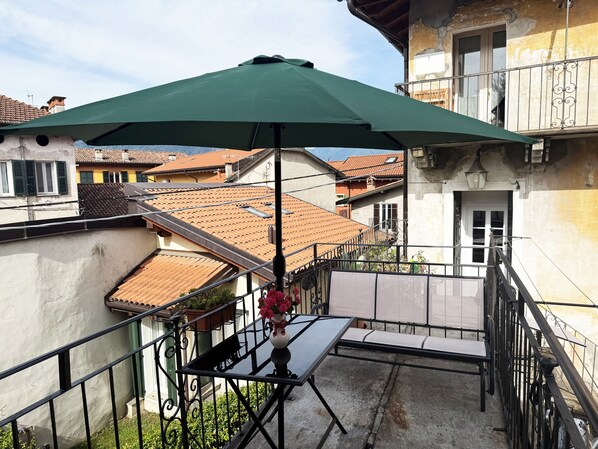 A balcony with a green umbrella, a table, and a chair. - 300 m from the lake: an entire house with a private parking space and terrace (Verbania)