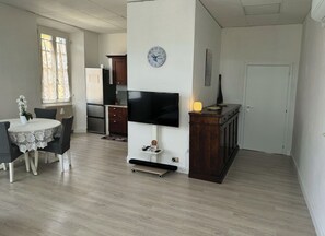 A dining area with a table and chairs, a kitchen with appliances, a flat-screen TV mounted on a wall, and a clock. - 300 m from the lake: an entire house with a private parking space and terrace (Verbania)