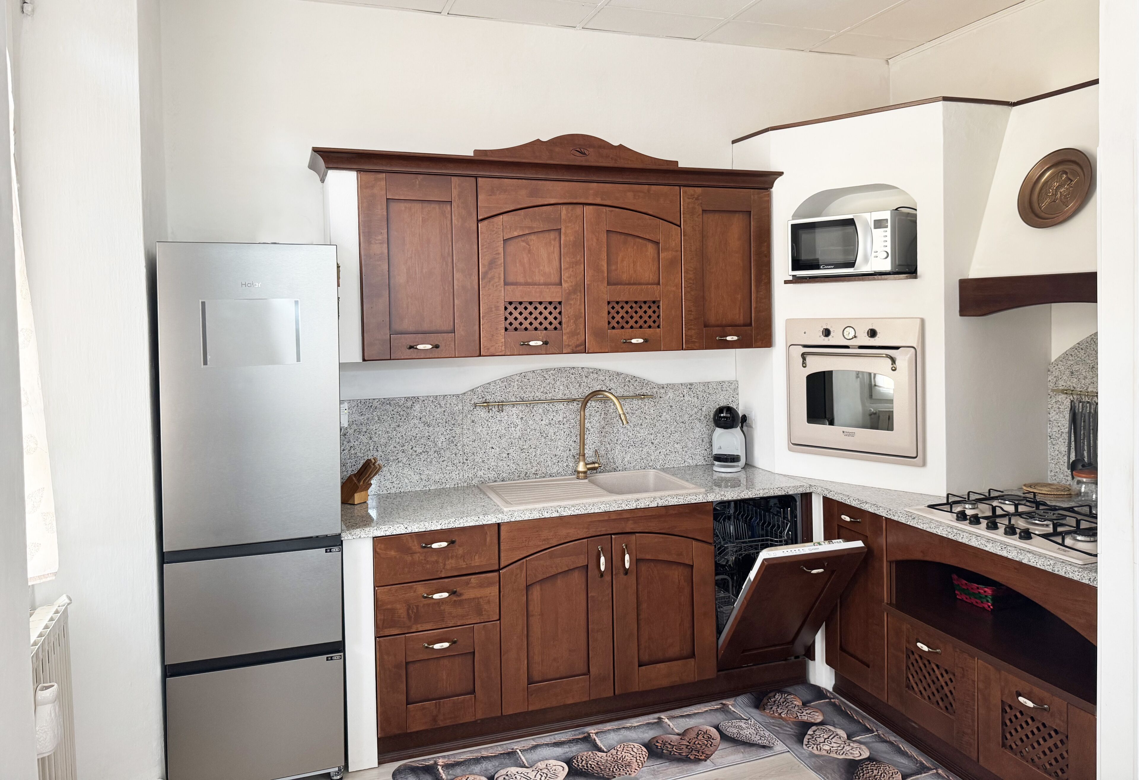 Una cocina con armarios de madera, un refrigerador de acero inoxidable, un microondas, un horno y una estufa a gas.