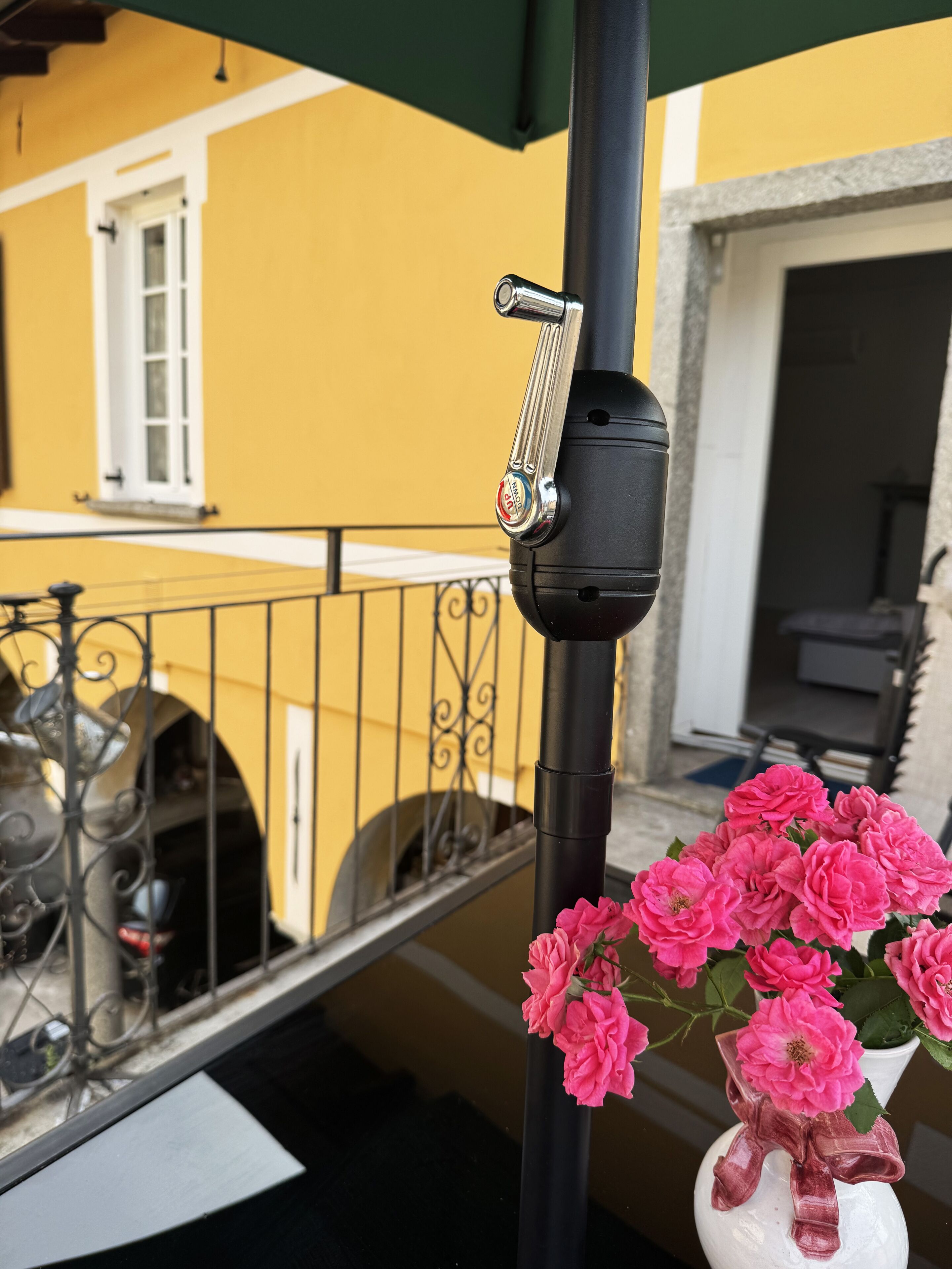 Uma varanda com guarda-corpo de metal, um poste preto com fechadura e um vaso com flores cor-de-rosa.