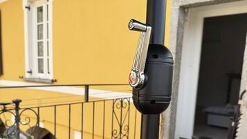 Uma varanda com guarda-corpo de metal, um poste preto com fechadura e um vaso com flores cor-de-rosa.