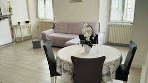 En matplats med ett runt bord, stolar, en vas med blommor, en soffa och ett element.