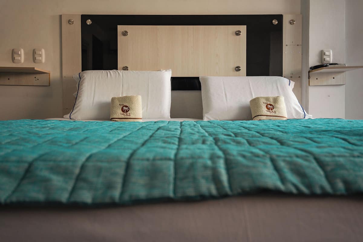 A neatly made bed with a teal bedspread, two pillows, and a headboard with a wooden panel.