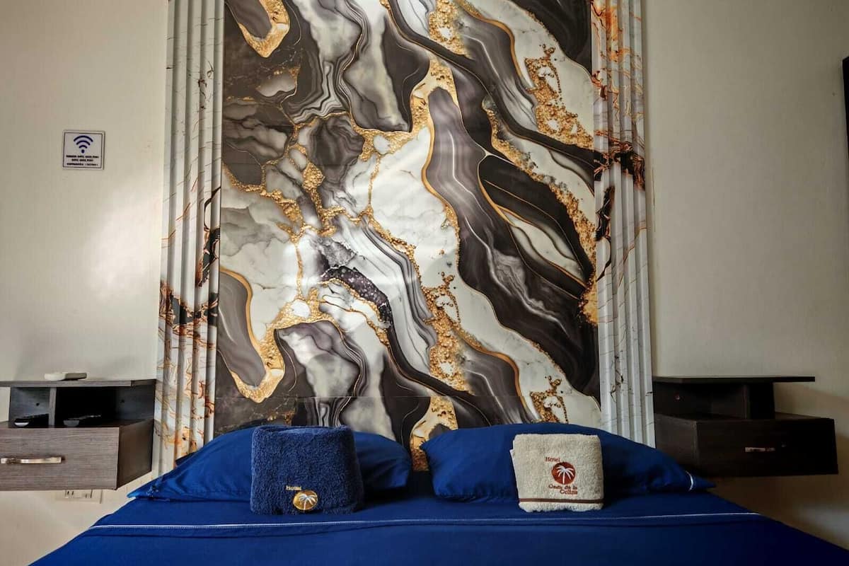 A hotel room with a bed, a nightstand, a TV, and a wall with a marble design.