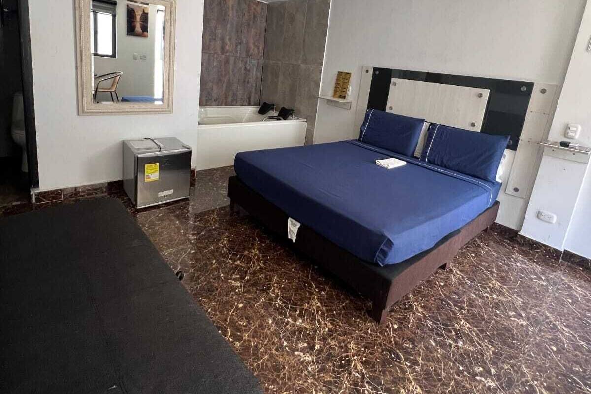 Ein Hotelzimmer mit Bett, Schreibtisch, Stuhl, einem kleinen Schrank und einem Spiegel.