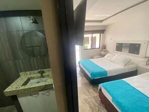 A hotel room with a bathroom, two beds, a window, and a mirror.