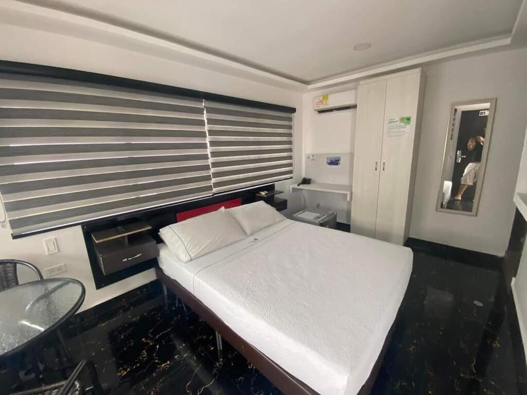 A hotel room with a bed, a small table, a chair, a wardrobe, and a window with blinds.