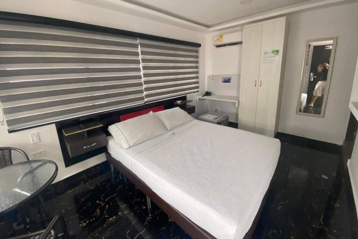 Ein Hotelzimmer mit Bett, kleinem Tisch, Stuhl, Kleiderschrank und einem Fenster mit Jalousien.