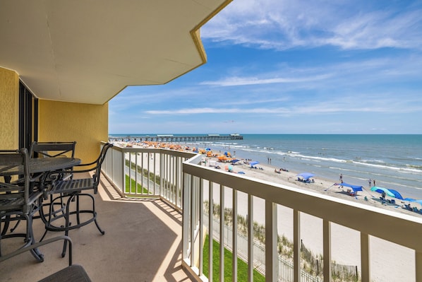 Ein Balkon mit Blick auf den Strand, einen Steg und einen klaren Himmel.