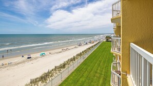 A beach view from a balcony with a clear sky, a sandy beach, and a grassy area. - Stay @ Ocean Potion - Oceanfront - Pools - Walkable to Center Street (Folly Beach)