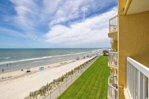 Blick auf einen Strand vom Balkon aus, mit blauem Himmel, Sandstrand und einer Rasenfläche.